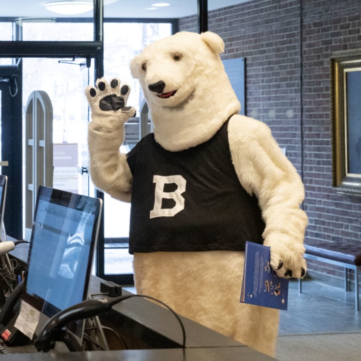 the Bowdoin polar bear mascot waves after checking out a book at the Circulation desk at H-L Library