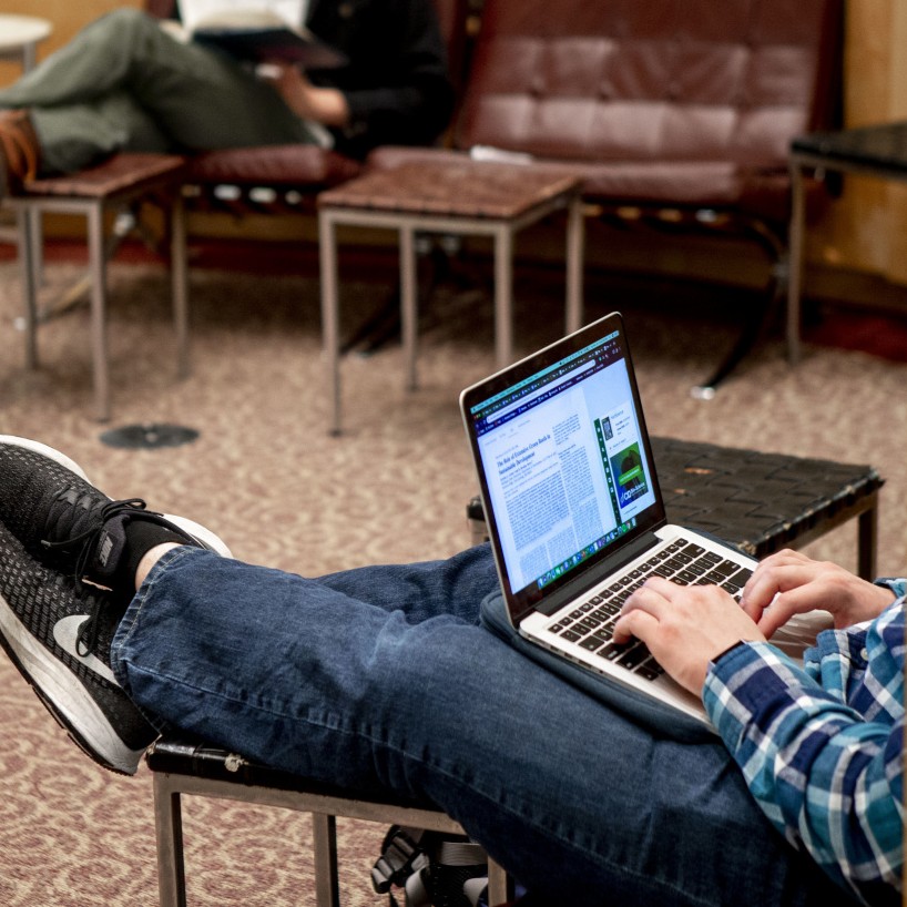 A student accesses a digital article from his laptop, sitting under the Calder sculpture on H-L first floor