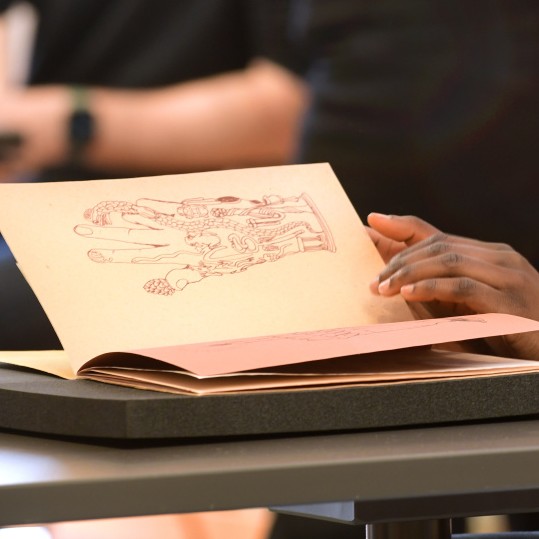 A student's hand turns the page of a book from Special Collections