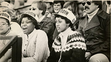 Undated. Students on bleachers watching an event. Man in the back row, center without sunglasses (out of focus) is Ed Burns (Class of ?1972).